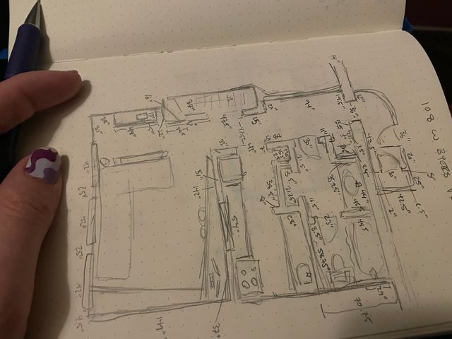 Hand holding a notebook and mechanical pencil, open to a page with a detailed sketch of my condo covered in measurements
