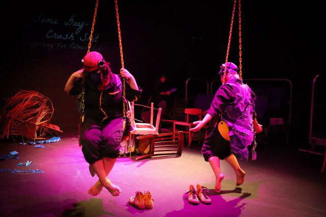 Bower bird dancers twisting and untwisting on yellow swings in purple theater lighting

