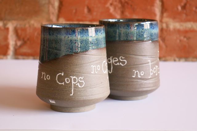Similar cups, but these say 'no cops, no cages, no borders' and have a blue glaze at the rim and inside.

